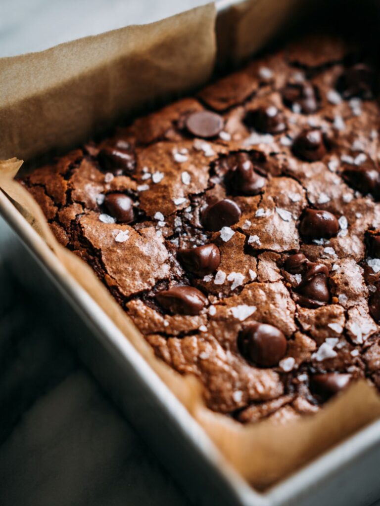 brookie bars fresh from oven in parchment-lined pan showing crackled brownie top and flaked sea salt