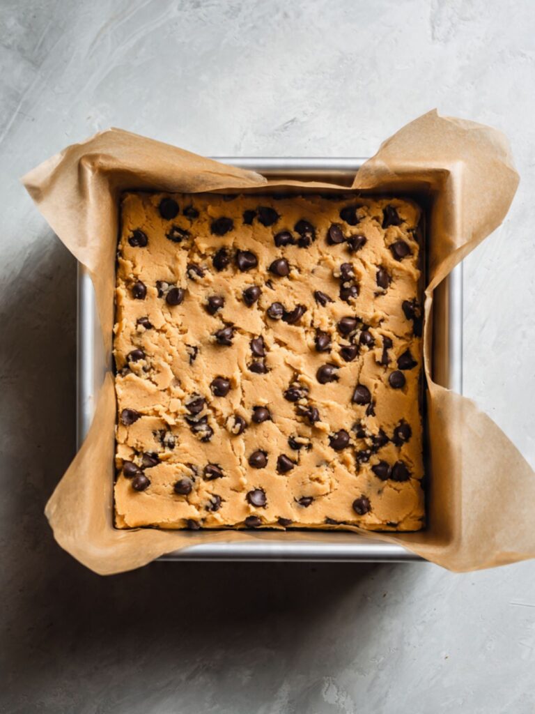 brookie cookie base dough pressed evenly into parchment-lined aluminum pan ready for par-baking