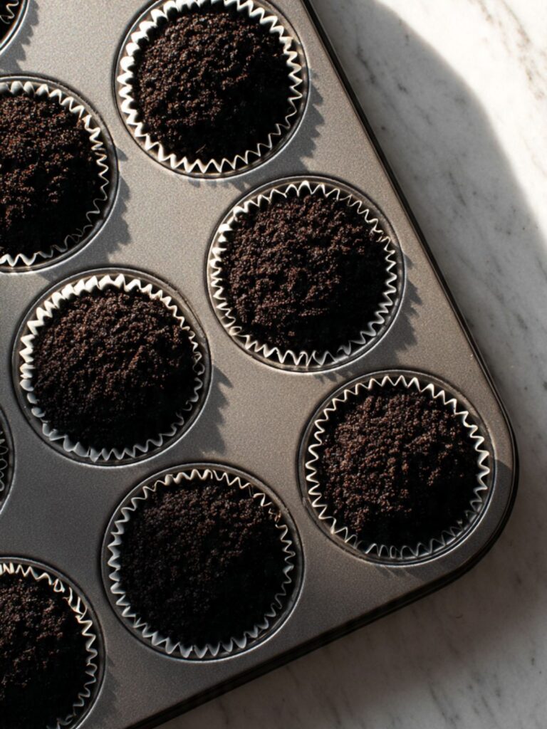 Oreo crust pressed into paper liners in muffin tin ready to chill before cookie dough filling is added