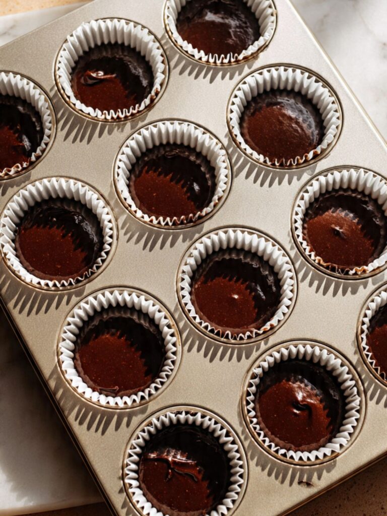 near-black chocolate brownie batter portioned into lined muffin tin for chocolate peppermint cookie cups