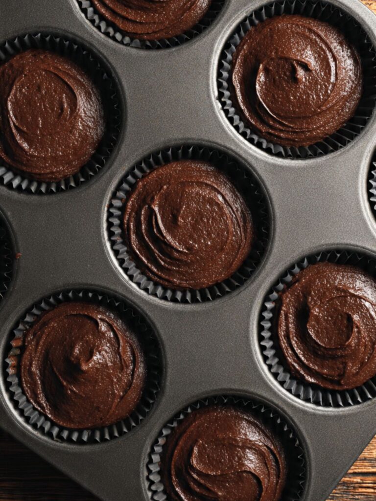 hot chocolate cupcake batter portioned into black paper liners in muffin tin, two-thirds full, dark batter