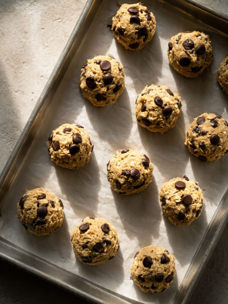 raw oatmeal chocolate chip cookie dough balls with chocolate chips pressed on top on parchment-lined baking sheet