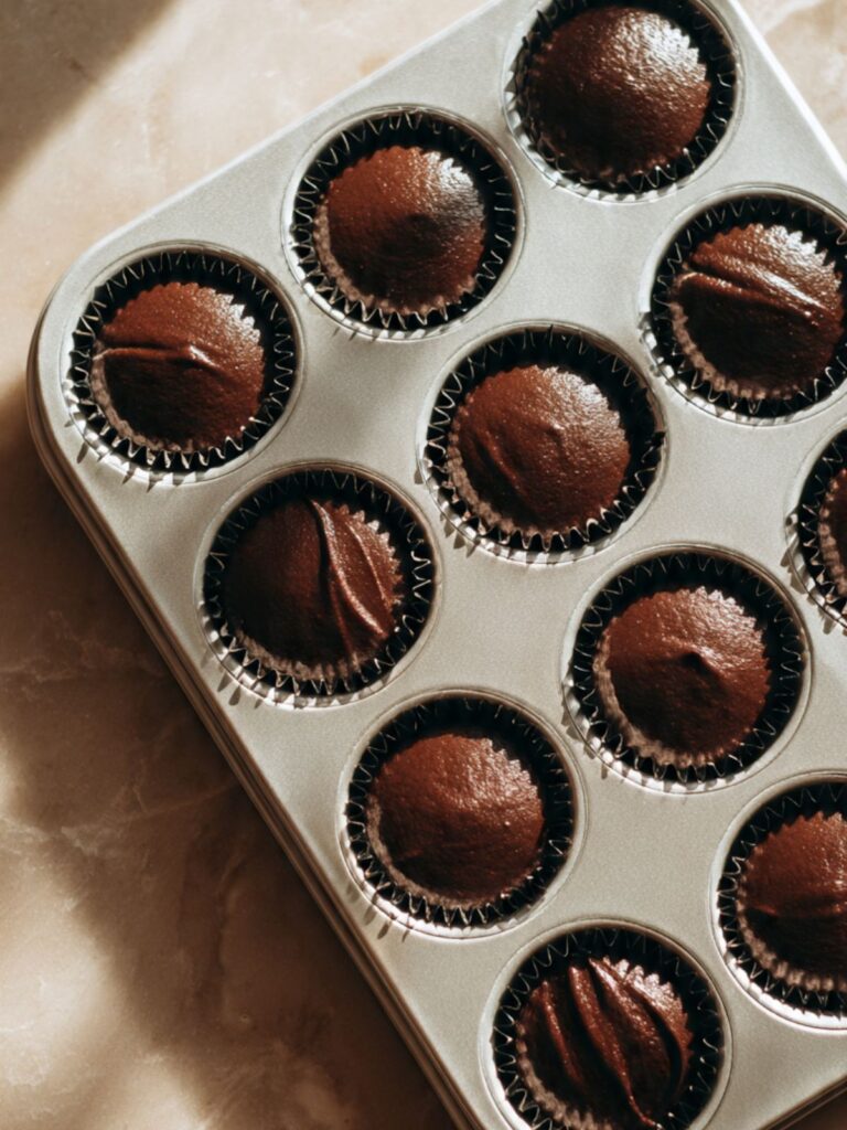 A 12-cup muffin tin filled with dark chocolate peppermint mocha cupcake batter in black foil liners ready to bake