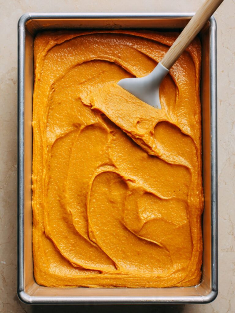 Deep orange pumpkin filling spread evenly in a greased 9x13 inch aluminum baking pan ready for cake mix layer