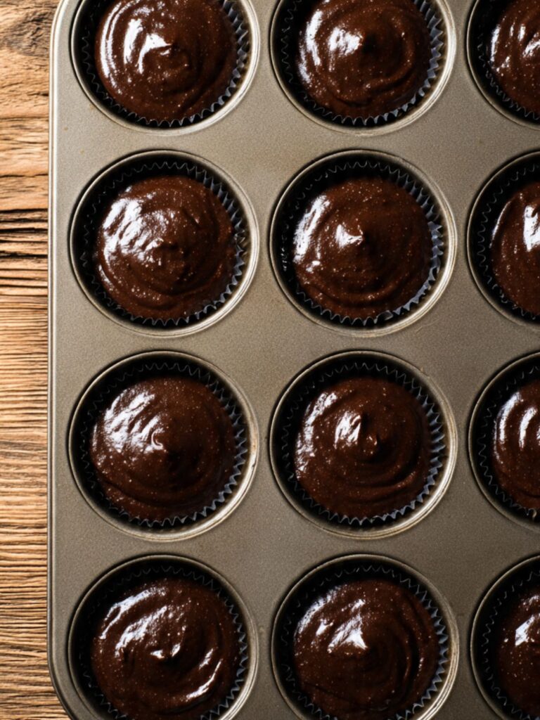 Dark chocolate cupcake batter portioned into dark-lined muffin tin, each cup filled two-thirds full
