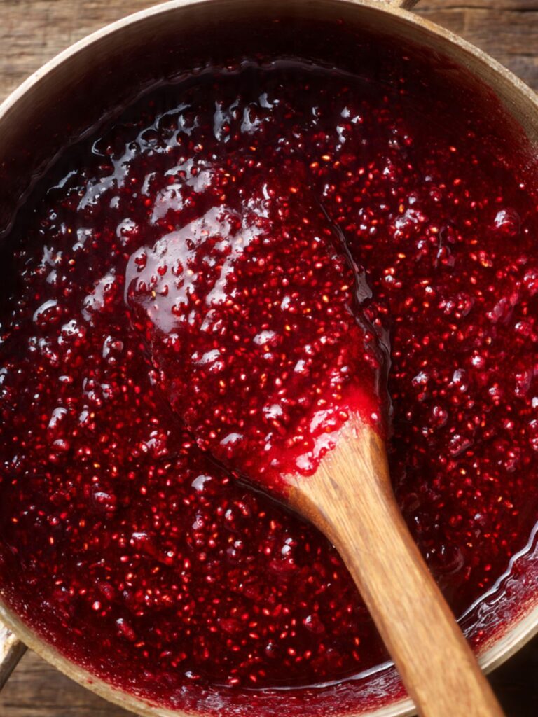 Raspberry compote bubbling in a medium saucepan on the stovetop, deep ruby red and glossy