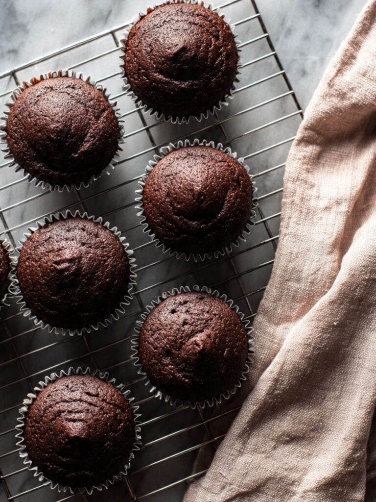 Dark chocolate raspberry lava cupcakes cooling on a wire rack, domed tops, dark liners