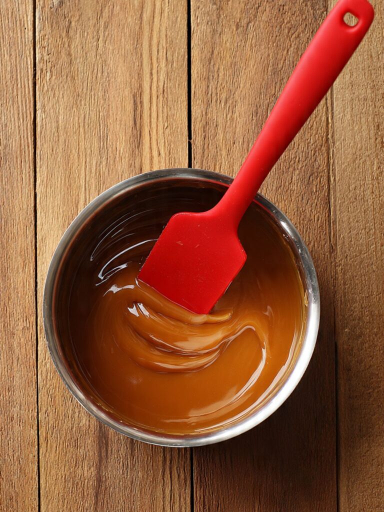 Smooth glossy melted caramel in a small silver saucepan with a silicone spatula, thick amber sauce ready to pour