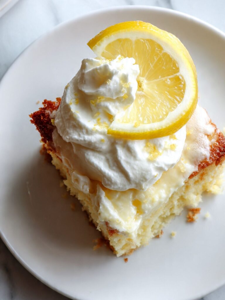 overhead view of lemon cream cheese dump cake slice showing dense creamy interior topped with whipped cream and lemon zest