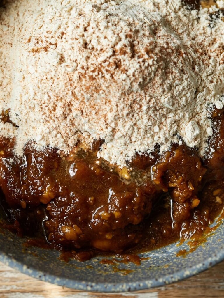 Flour and spice mixture poured over wet brown butter pumpkin cookie base in a mixing bowl before folding