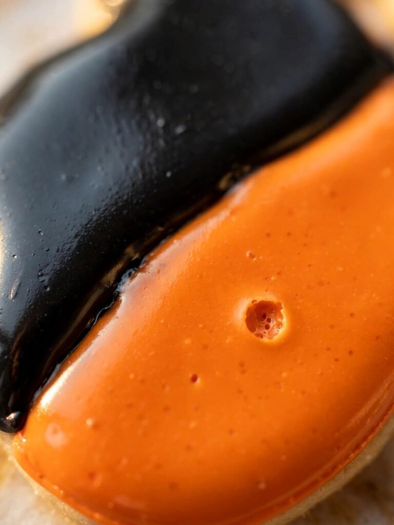Extreme close-up of glossy, hardened black and orange royal icing texture on a Halloween sugar cookie